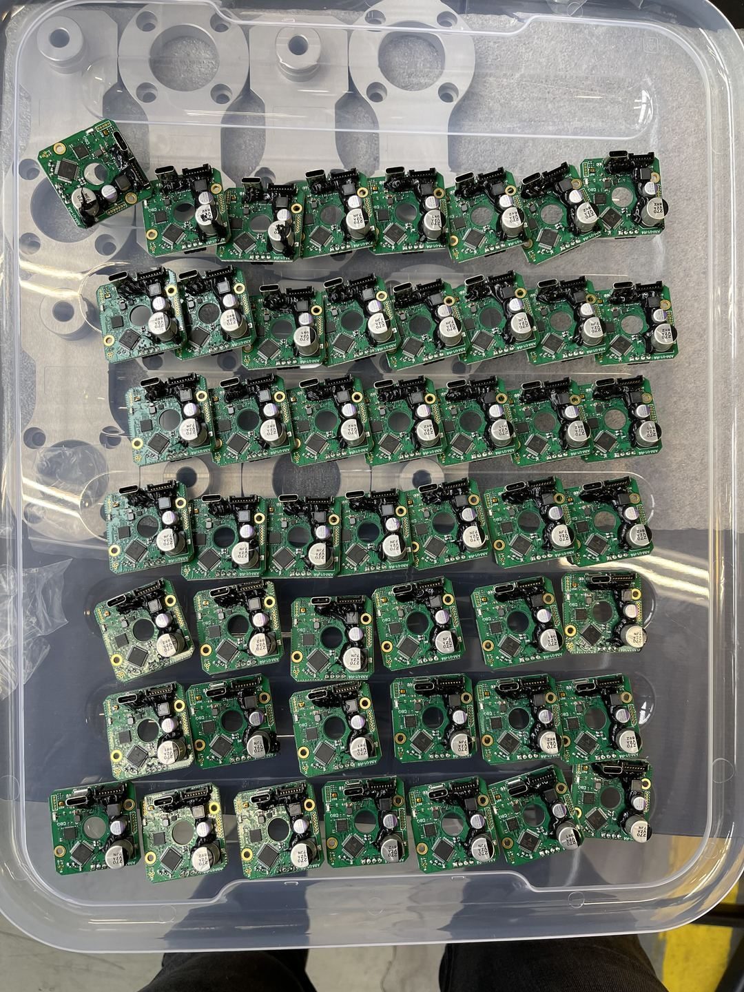 Production batch of ~50 custom AimRobotics PCBAs in a tray — motor drivers, capacitors, connectors, conformal coating