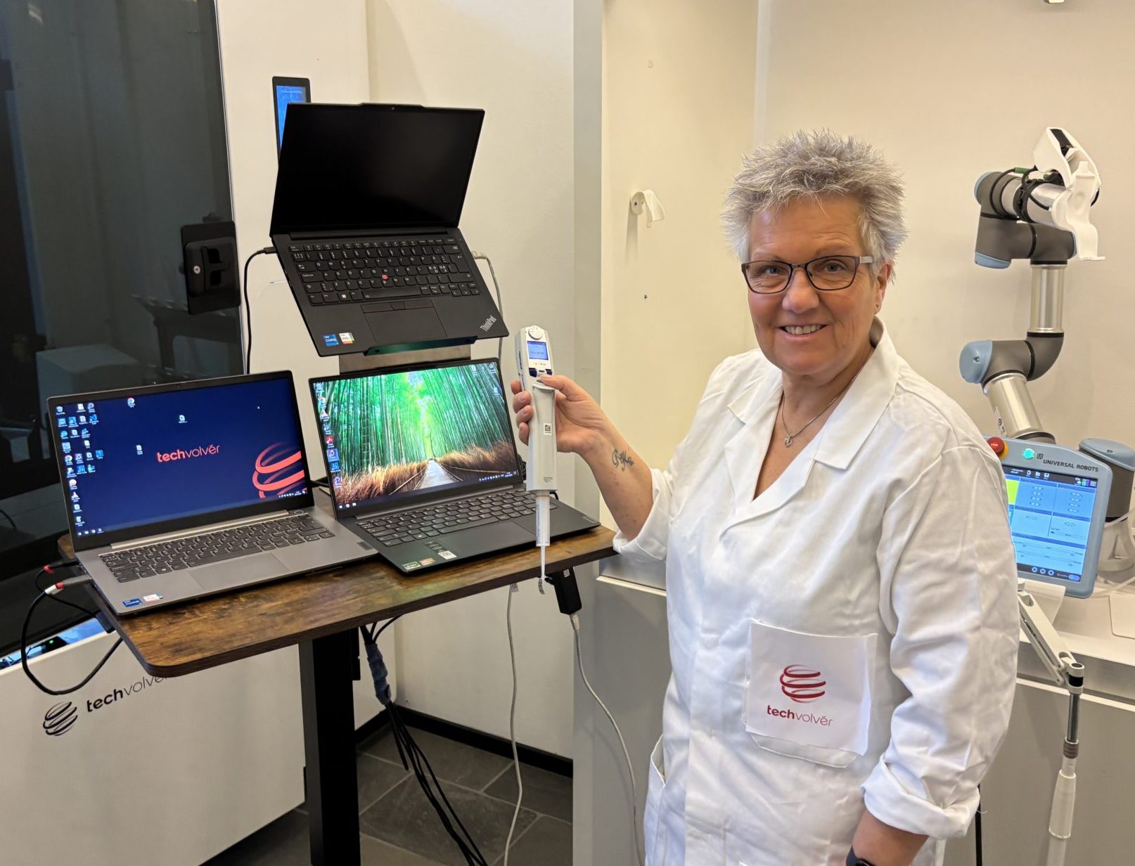 TechVolver team member holding a calibrated pipette next to the Calvolver system with UR robot arm and control laptops